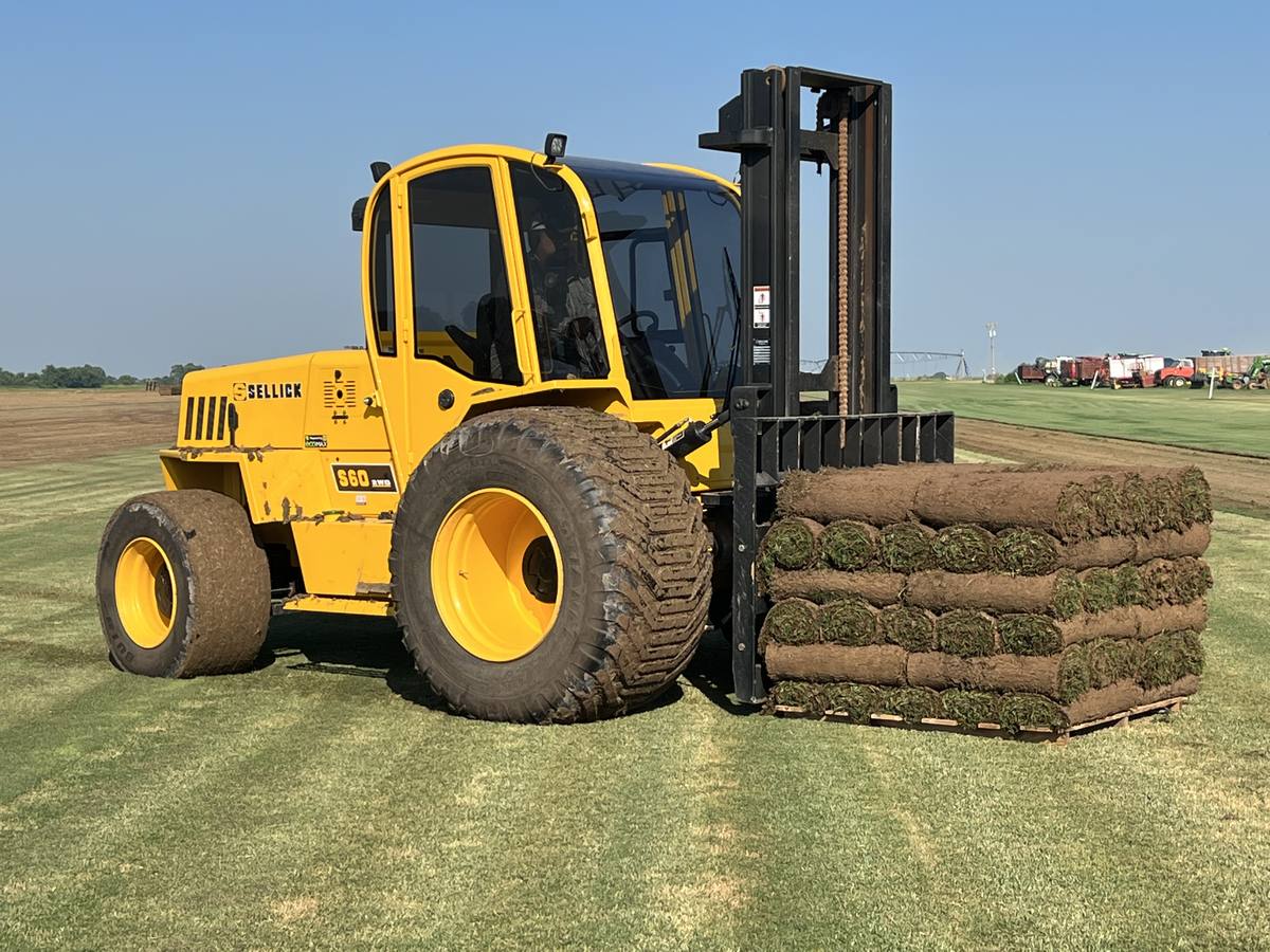 Sellick forklift carrying a pallet of fresh-cut sod rolls across the field